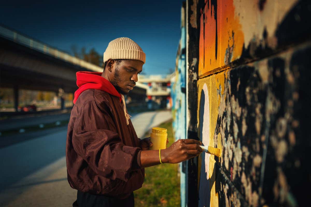 Closeup side view of a young African American man creating street art drawing on the wall.